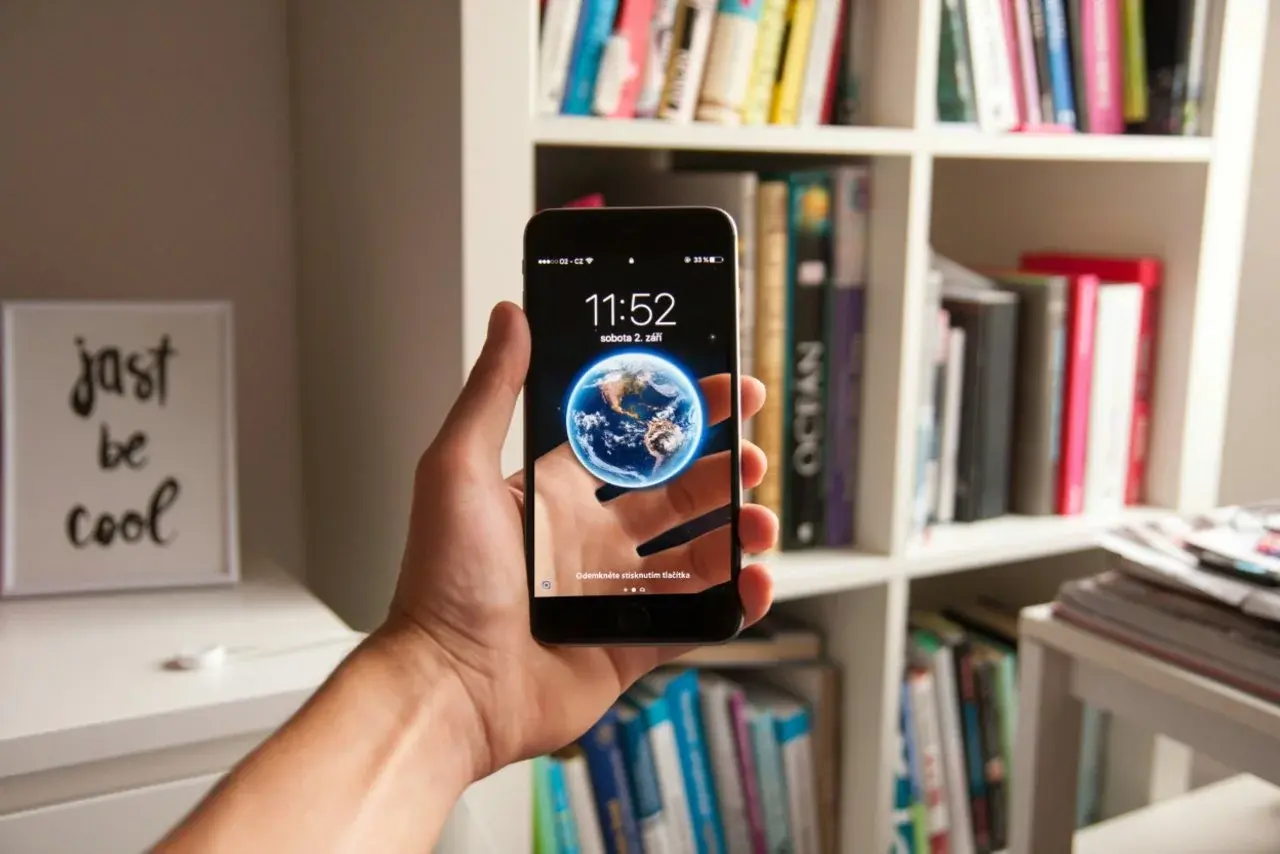 Hand hält Smartphone mit Erdball‑Wallpaper.