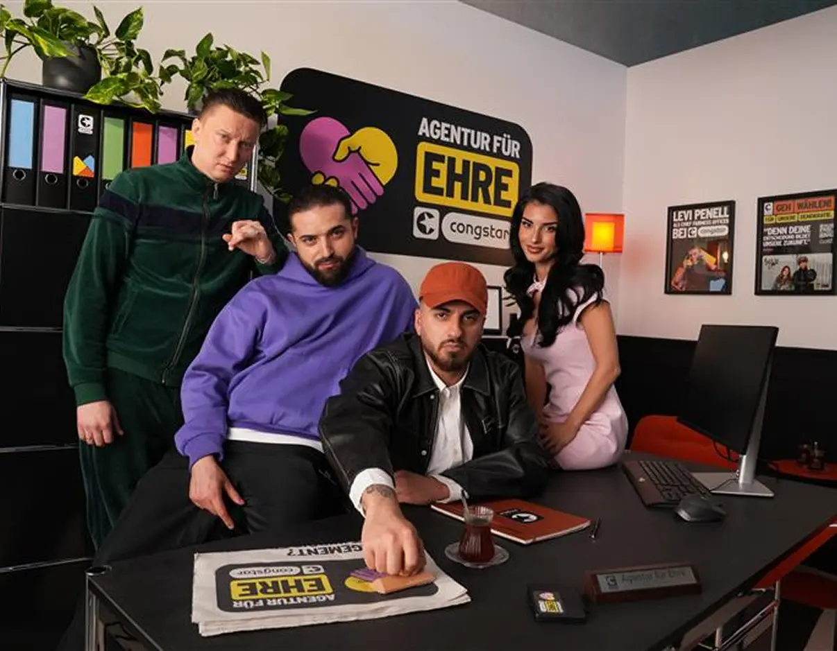 Creator*innen Team in einem Büro mit dem Logo „Agentur für Ehre" von congstar im Hintergrund.