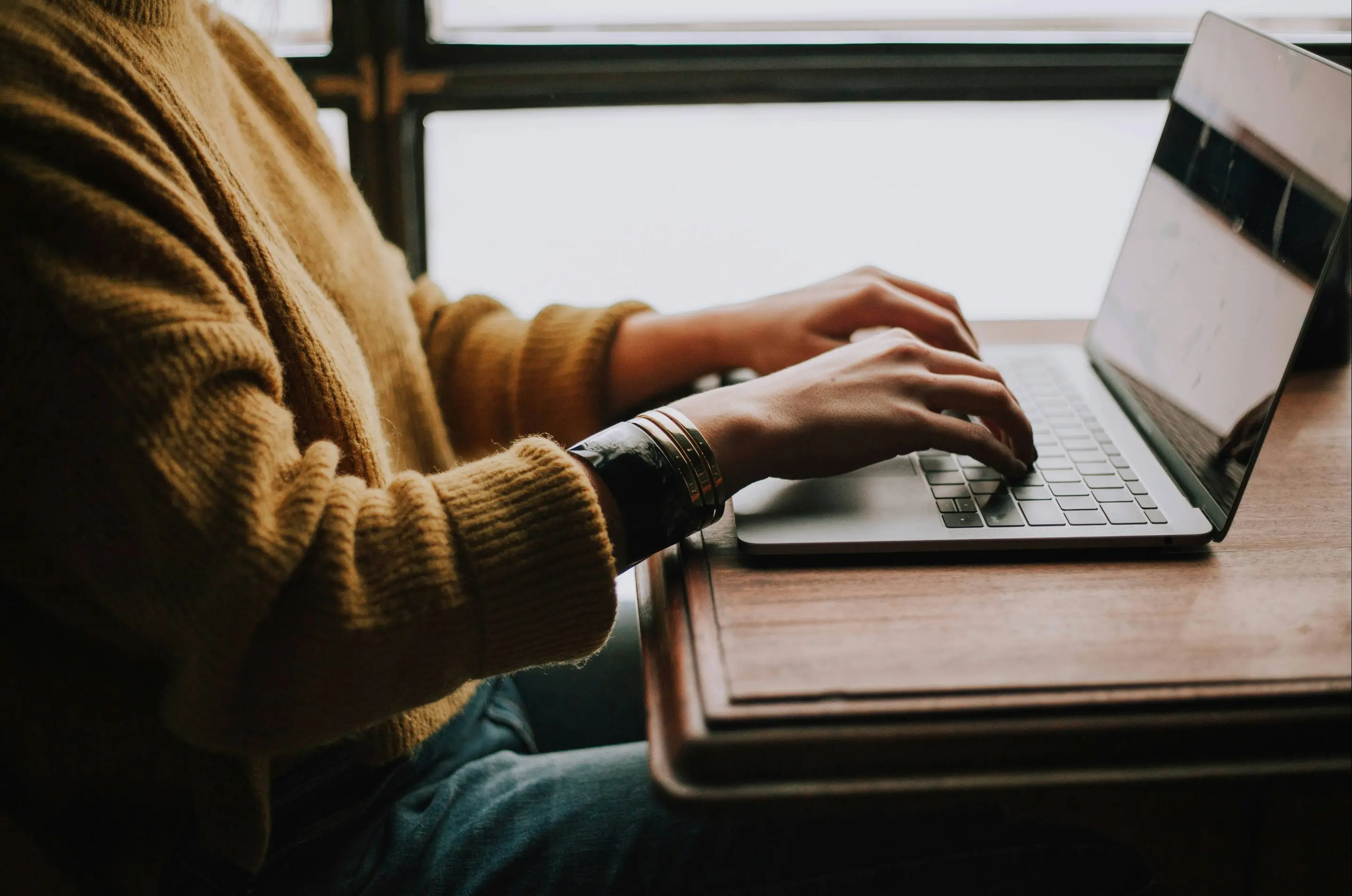 Person sitzt am Tisch und tippt auf dem Laptop