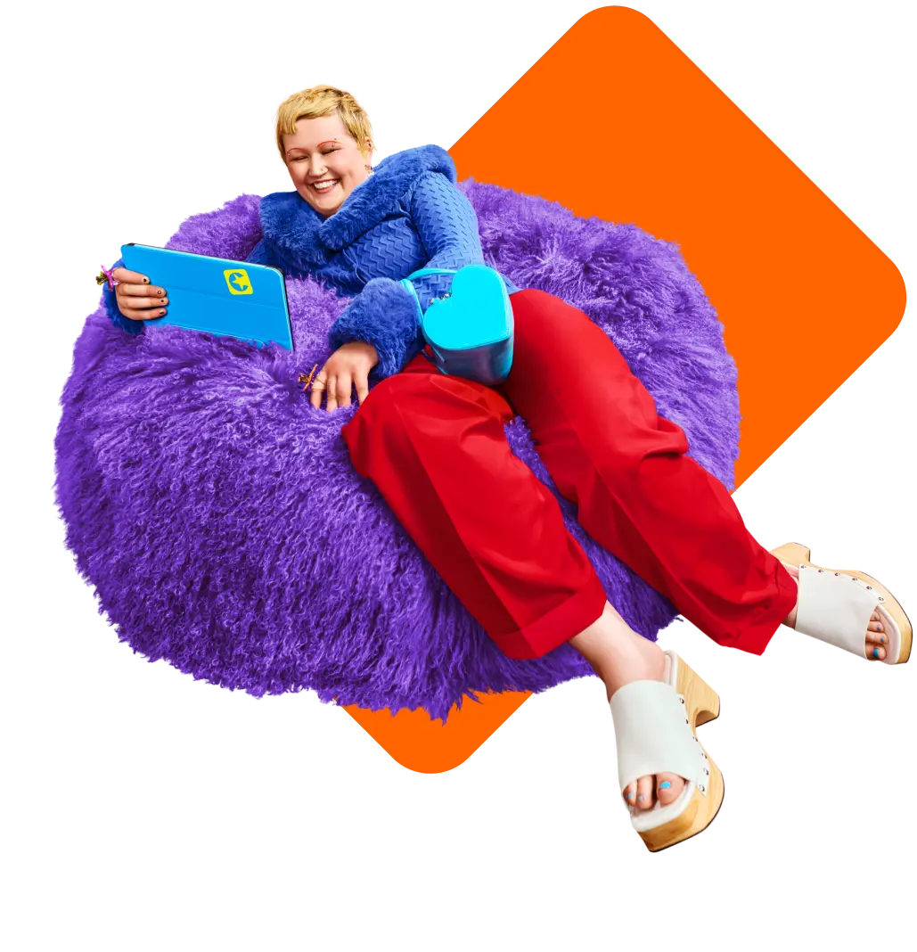 Lächelnde Person sitzt mit Tablet auf einem Sitzkissen.