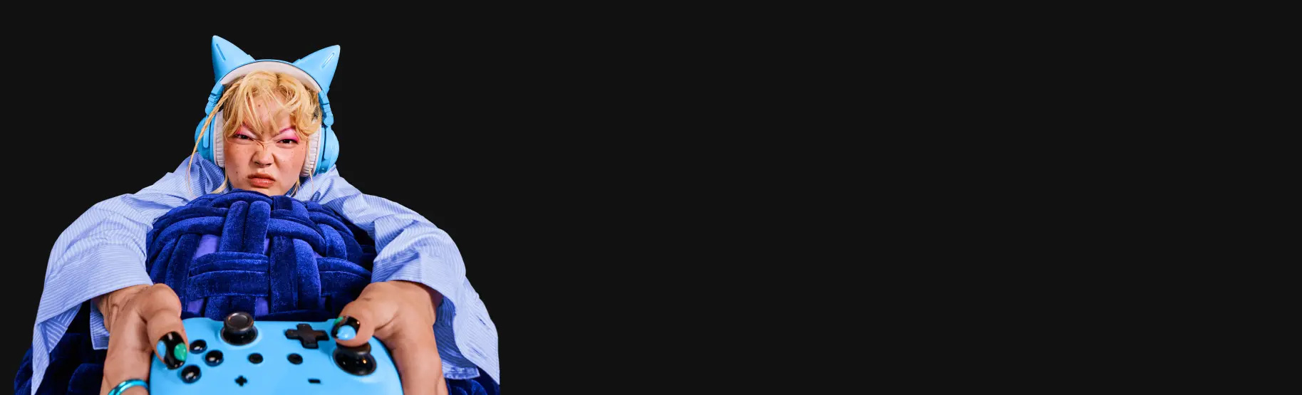 Eine Person trägt ein blaues Kostüm mit Katzenohren und schaut konzentriert. Der Hintergrund ist schwarz.