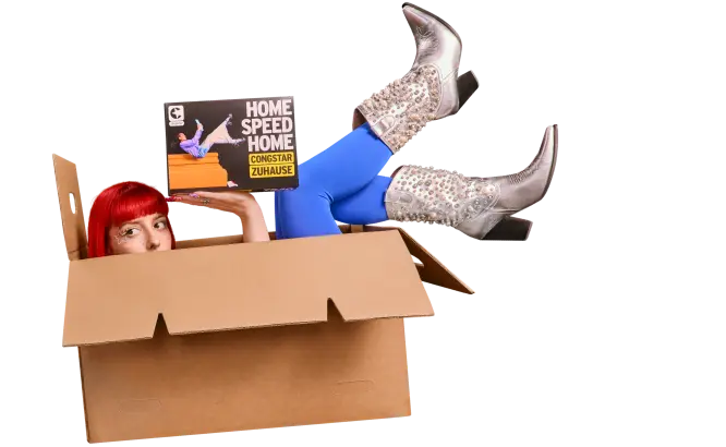 Person sitzt in einem Umzugskarton und hält eine Produktverpackung mit der Aufschrift „Home Speed Home – congstar Zuhause" hoch.