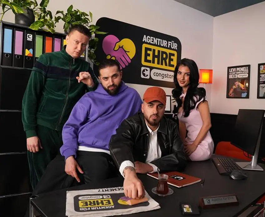 Creator*innen Team in einem Büro mit dem Logo „Agentur für Ehre" von congstar im Hintergrund.