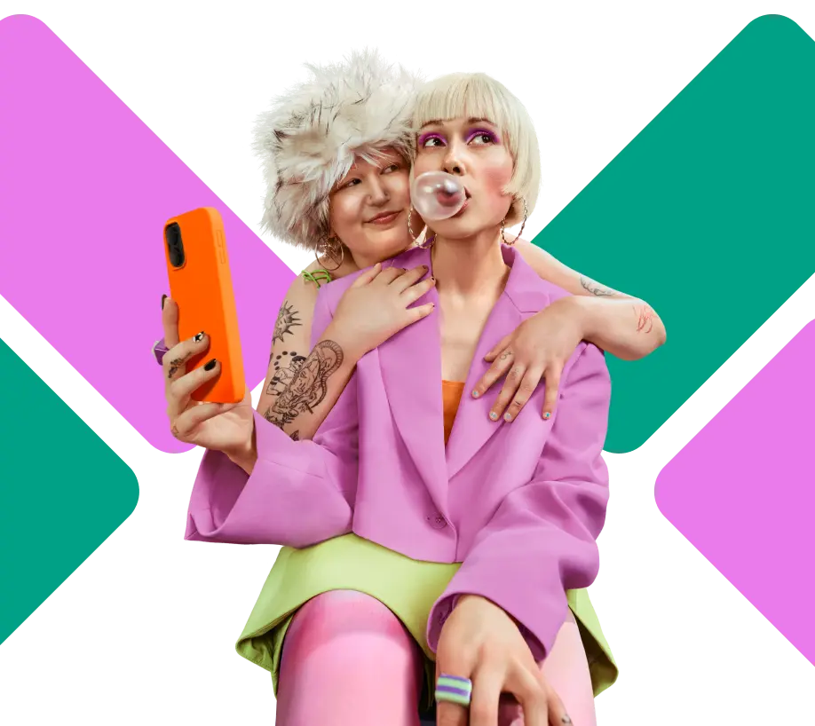 Zwei Personen in bunten Outfits posieren zusammen – eine hält ein Smartphone mit orangefarbener Hülle, die andere pustet eine Kaugummiblase.