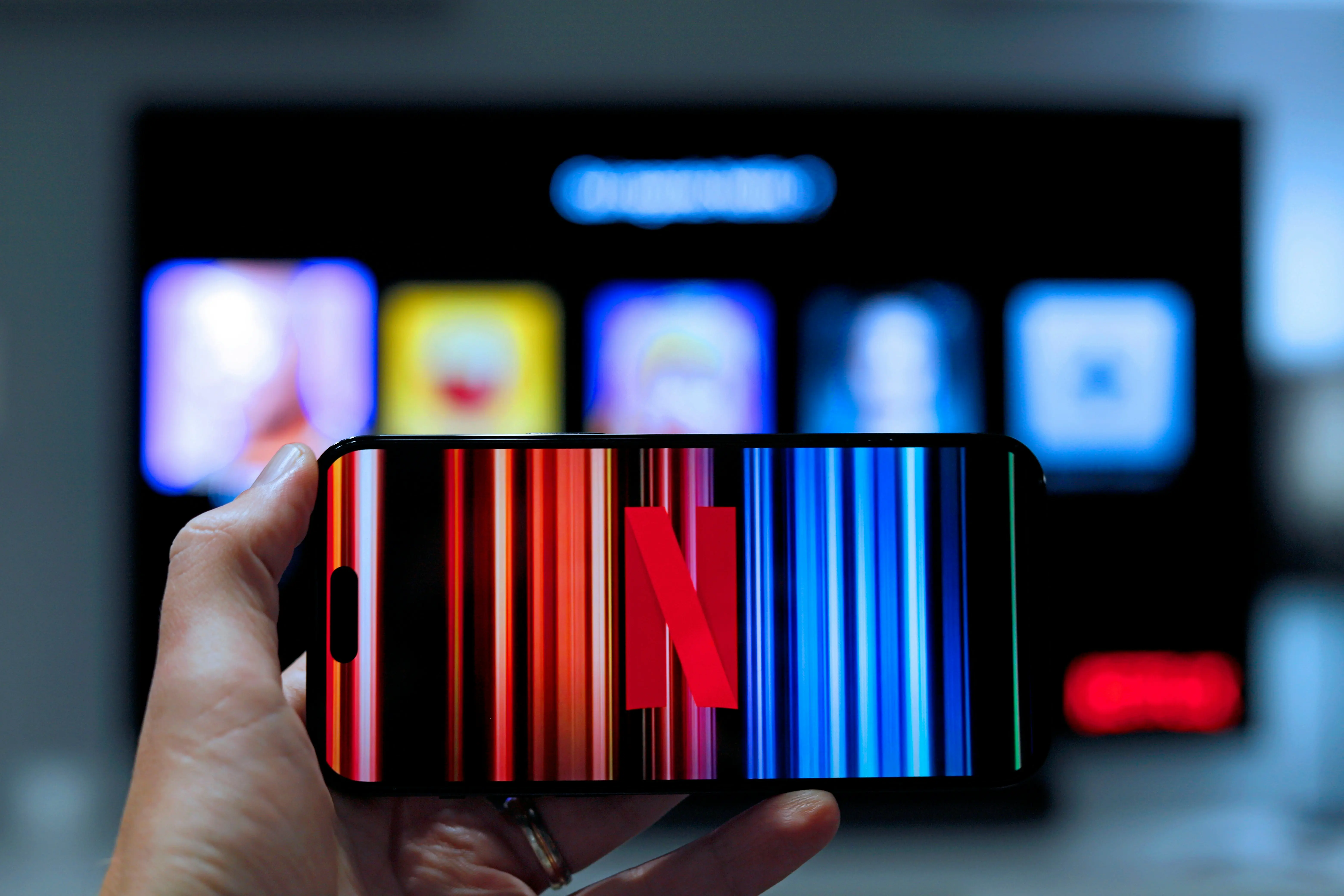 Person hält Handy mit Netflix drauf vor einen TV