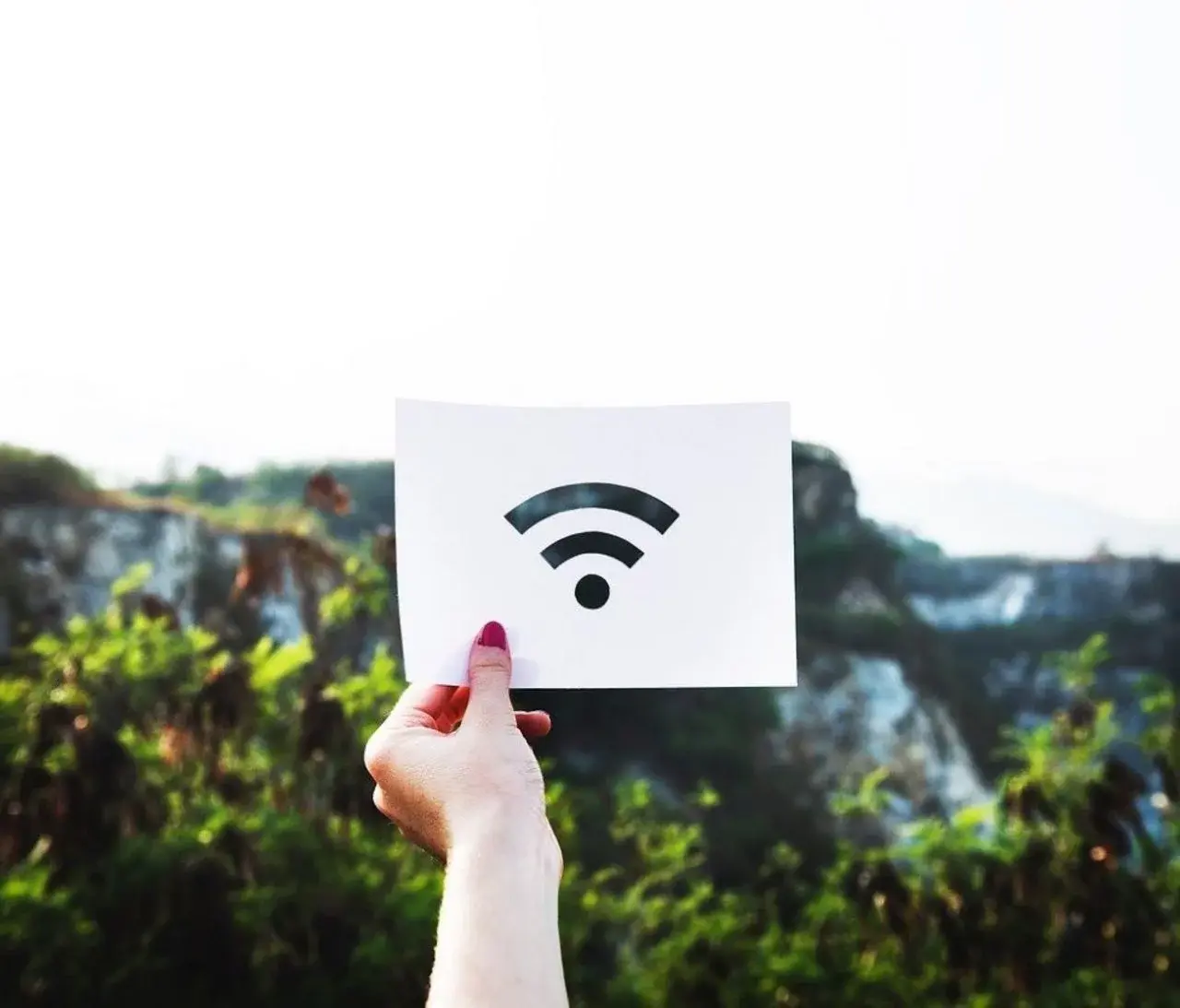 Hand hält Karte mit WLAN-Symbol vor grüner Landschaft im Freien.