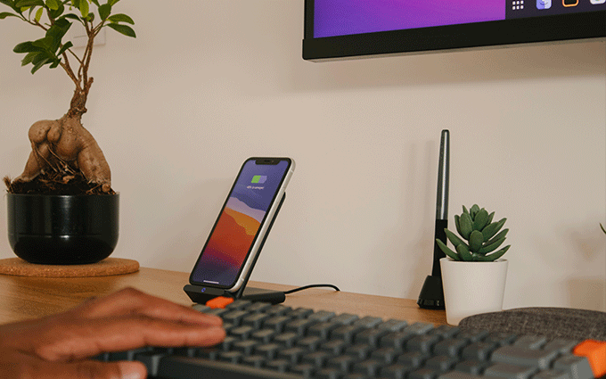Person tippt auf einer Tastatur und im Hintergrund steht ein Handy auf einer wireless-chargering-station