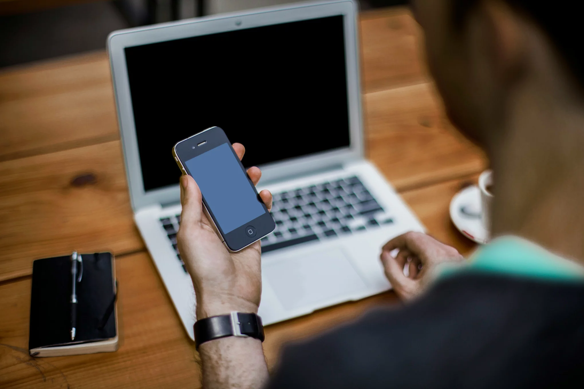 Person hält Handy in der Hand und sitzt vor einem Laptop