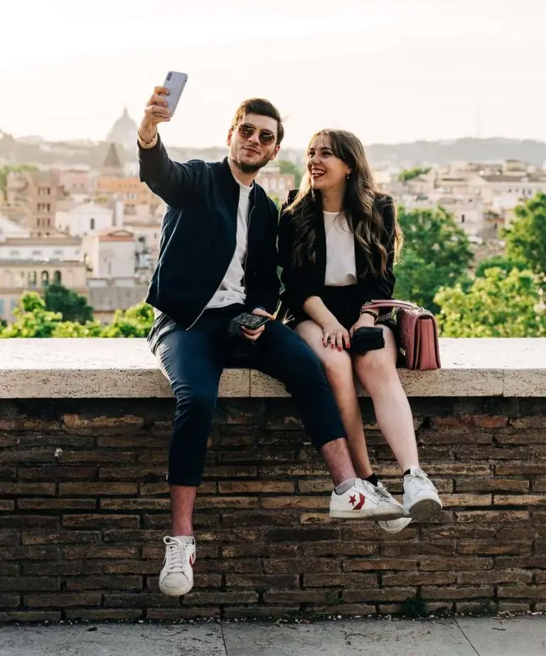 Pärchen sitzt auf einer Mauer und macht gemeinsam ein Selfie